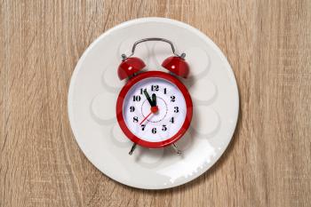Plate with alarm clock with five minutes to twelve o'clock on the dial. Lunch time concept