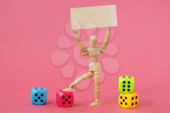 Wooden man with a blank banner and colored dices on the pink background