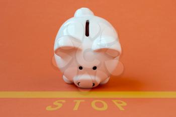 Piggy bank at the edge of a yellow line with a yellow print of the word STOP. Conceptual image.