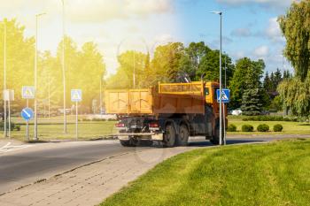 Heavy industrial dump truck maneuvering in the narrow pass of a landscaped roundabout 