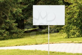 Empty white sign on the street with green nature on background