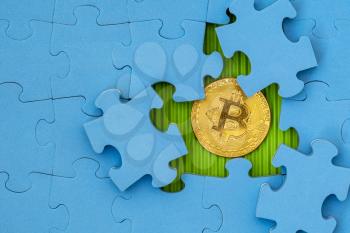 Blue jigsaw puzzle with golden bitcoin underneath 