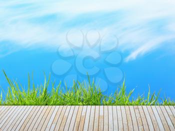 Green grass with wooden pier over blue sky