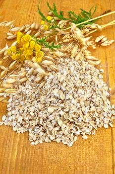Oat flakes with yellow wildflowers the tansy and stalks of oats on a wooden board