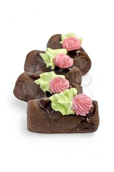 Several chocolate sponge cake with chocolate icing, flower and leaf out of cream isolated on a white background