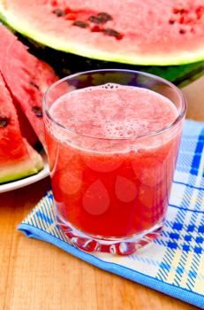 Watermelon juice with a slice of watermelon on a blue checkered napkin against a wooden board