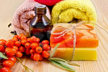 Oil in a bottle, two homemade soap, towels, twig and berries of sea buckthorn on a wooden board