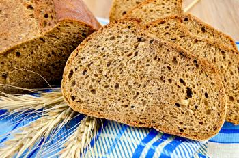 A few slices of rye bread, three rye spikelets on a blue napkin against a wooden board