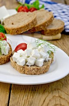 Slices of bread with feta cheese, tomato and dill on a plate, napkin on a wooden board