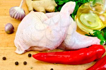 Two chicken legs, vegetable oil in a bottle, red hot pepper, ginger, garlic on a wooden board