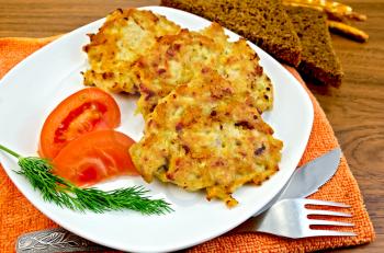 Fritters of minced chicken on a white plate with tomato and dill, knife, fork, napkin orange, rye bread on a wooden board