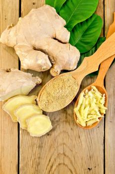 Grated and ground ginger in two wooden spoons, ginger root, green leaves on the background of wooden board