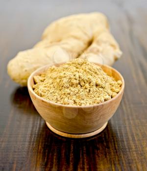 Wooden bowl with powdered ginger, ginger root on the background of wooden board