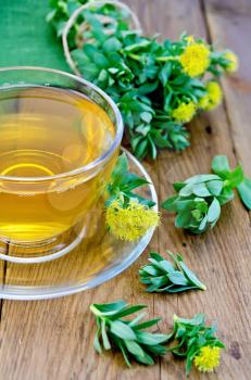 Healing herbal tea in a glass cup, flowers Rhodiola rosea, green napkin on a background of wooden boards