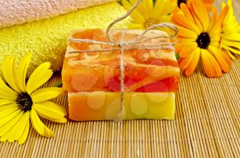Two bars of homemade soap yellow and orange, towels, marigold flowers on a background of bamboo napkins