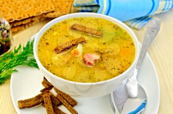 Pea soup with rye croutons in a bowl and on a plate, spoon, pepper, bread, napkin against a wooden board