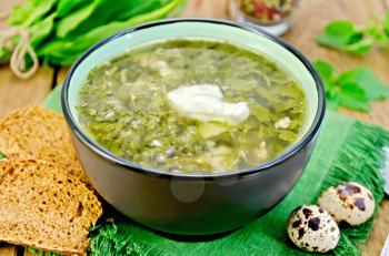 Green soup of sorrel, nettle and spinach in a bowl, quail eggs, bread, pepper against a wooden board