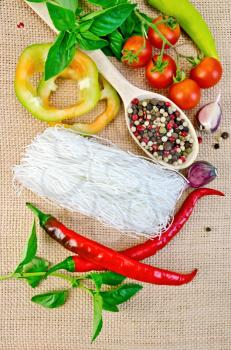 Rice noodles thin, tomatoes, different peppers, garlic, basil on a background of sack cloth