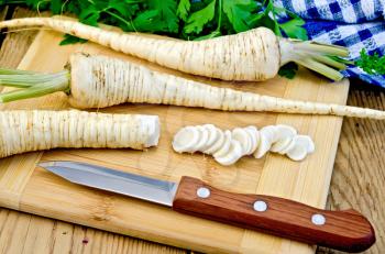 Parsley roots whole and sliced with green haulm, knife, napkin on the background of wooden boards