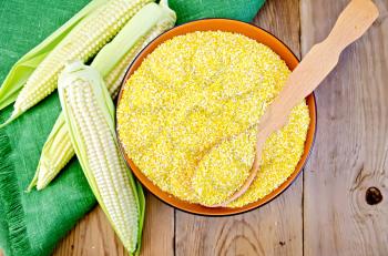 Corn grits in a bowl with a spoon, corn on the cob on a napkin on the background of wooden boards