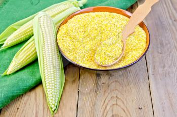 Corn grits in a bowl with a spoon, corn on the cob on a green napkin on the background of wooden boards