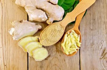 Grated and ground ginger in two wooden spoons, ginger root, green leaves on wooden board