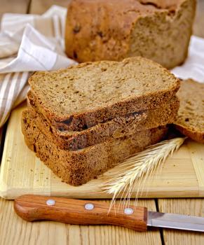 A stack of slices of rye homemade bread with a knife and rye spikelet on plate, napkin, loaf of bread on a wooden board
