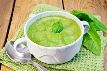Green soup puree in a bowl with green leaf spinach, spoon on a napkin on the background of wooden boards