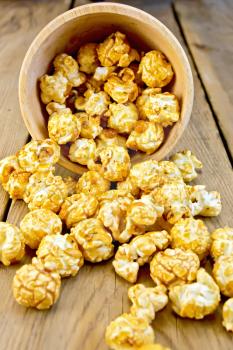 Caramel popcorn poured out of a wooden bowl on a wooden boards background