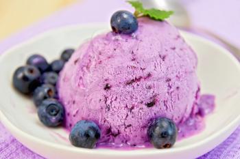 Blueberry ice cream with mint leaves in a bowl with berries on a background of purple cloth and wooden boards