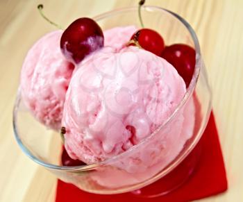Cherry ice cream in a glass bowl on a red paper napkin on the background of wooden boards