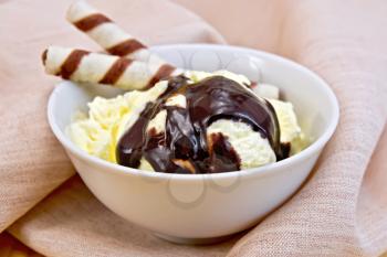 Vanilla ice cream in a bowl with wafer rolls and chocolate syrup on a napkin on the background of wooden boards