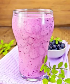 Milkshake with blueberries in a glass on a purple napkin, blueberries on a wooden boards background