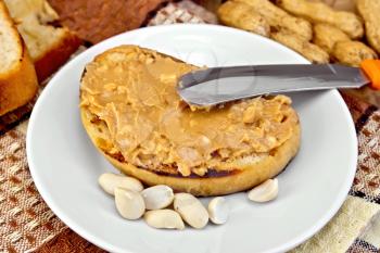 Sandwich with peanut butter in a bowl with nuts and a knife on a napkin, bread on the background of wooden boards