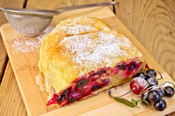 Strudel with black currant and cherry, metal sieve, powdered sugar on a wooden boards background