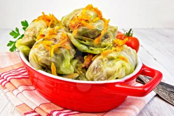 Stuffed cabbage meat in cabbage leaves with roasted carrots in a roasting pan on a red napkin, tomatoes, knife, fork on a lighter background board