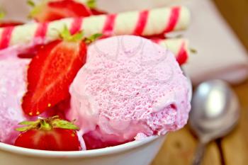 Strawberry ice cream in a white bowl with strawberries and wafer rolls, napkin on wooden board