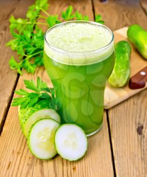 Cucumber juice in a tall glass, cucumbers, parsley and knife on a wooden boards background