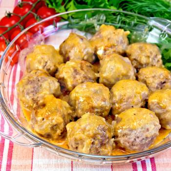 Meatballs with sauce in a glass pan, tomatoes, parsley, dill on background linen tablecloth