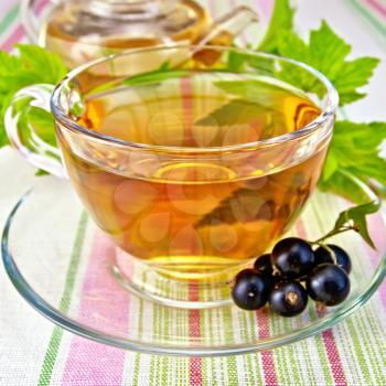 Tea in a glass cup and teapot, berries and green leaves of black currant on a background linen tablecloths