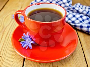 Chicory drink in red cup with flower, napkin on a wooden boards background
