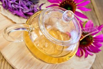 Herbal tea in a glass teapot, fresh and dried flowers of Echinacea on a wooden boards background