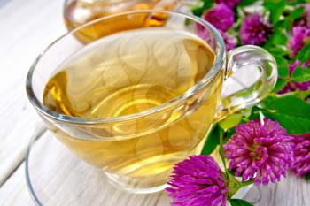 Herbal tea with clover flowers in a glass cup on a background of pale wooden plank