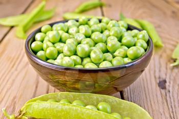 Green peas in a brown bowl, pea pods on a wooden board