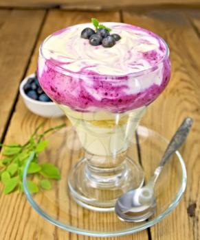 Dessert milk with blueberry, cornflakes, curd, spoon in a glassware on a wooden board