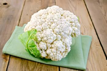 White cauliflower with green leaf on a napkin on a wooden boards background