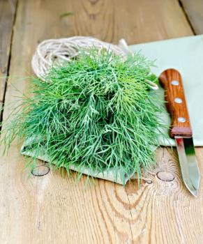 Dill fresh green with a skein of twine, knife, napkin on a wooden boards background