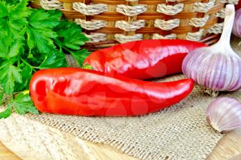 Two red hot pepper pod, a bunch of parsley, garlic, wicker basket on a background of burlap cloth and wooden planks