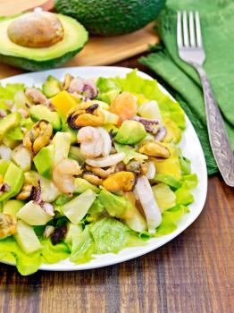 Salad with shrimps, octopus, mussels and calamari with avocado, lettuce, pineapple in plates, napkin, fork, sliced avocado on a background of dark wooden boards