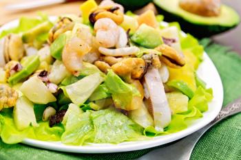 Salad with shrimps, octopus, mussels and calamari with avocado, lettuce, pineapple in plate on a green napkin, fork on the background dark wooden boards